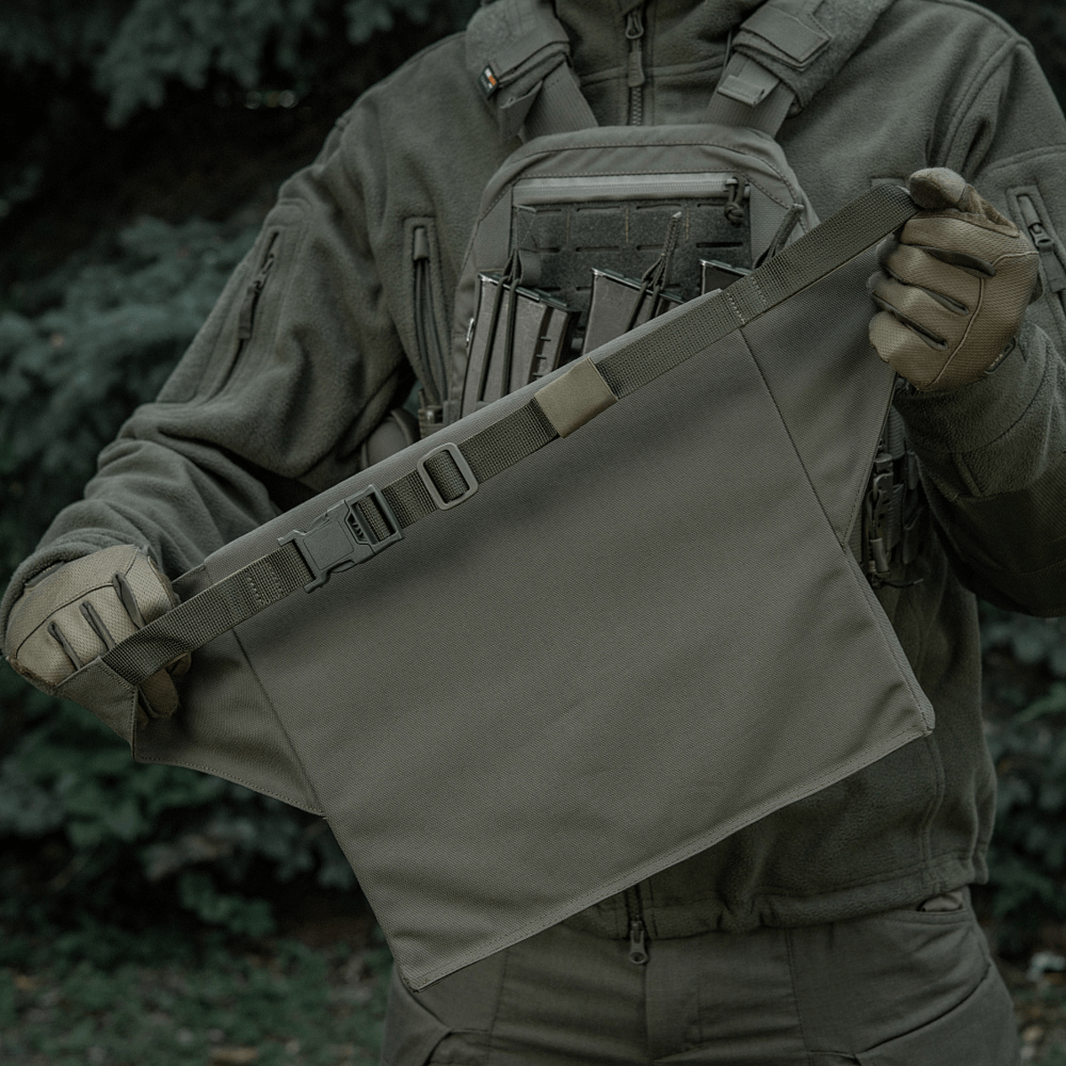M-Tac Siddeunderlag med bælte i grøn farve, holdt af en person i militærudrustning, ideel til udendørs aktiviteter.