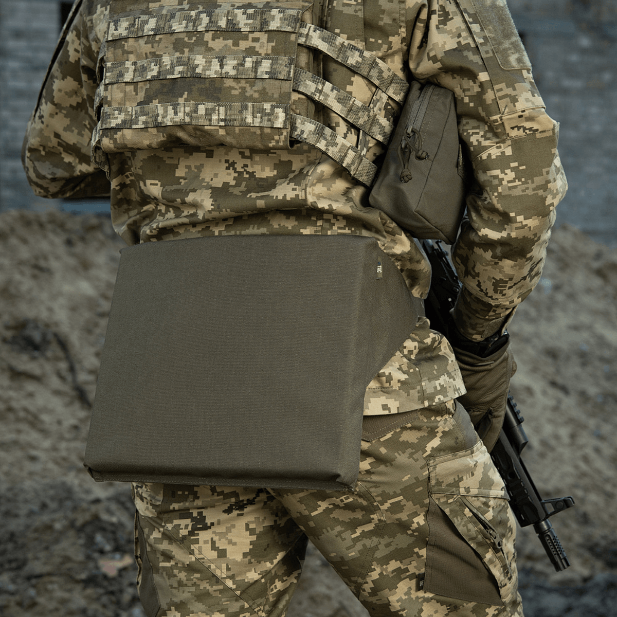 Soldat med M-Tac Siddeunderlag med bælte i camouflagetøj, klar til mission på groft terræn.