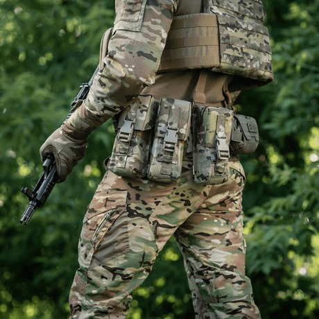 Mann i kamuflasjeutstyr iført M-Tac dobbelt magasinlomme med Fastex-lukking, klar for militære og sikkerhetsaktiviteter i skogen