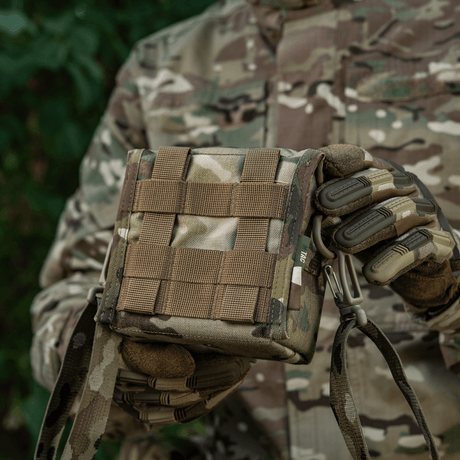 M-Tac-veske for nattkikkert PVS-14 i kamuflasje, holdt av person i skogmiljø, med Fastex-lukning og elastiske stropper for sikker oppbevaring.