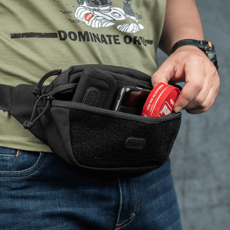Person bruker M-Tac Tactical Waist Bag Gen.II Elite til oppbevaring, viser holdbarhet og funksjonalitet i svart design, perfekt for daglige aktiviteter.