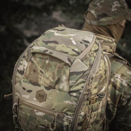 M-Tac Ryggsekk Large Gen.III Elite i camouflage mønster bæres av person iført militærtøy i skogområde.