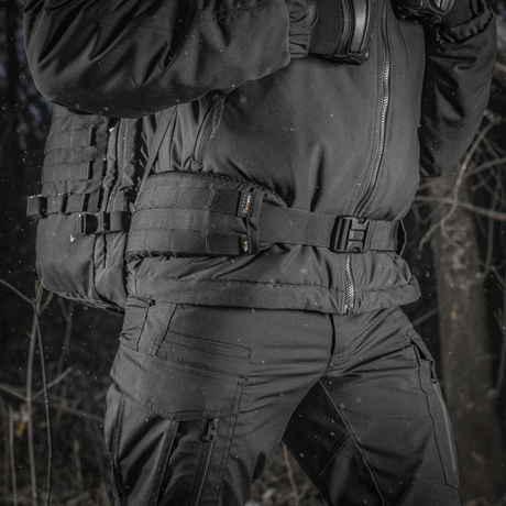 M-Tac Ryggsekk Gen.II Elite Large båret av en person i vintertøy i en skog, laget av slitesterk Cordura for maksimal holdbarhet.