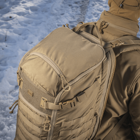 M-Tac Ryggsekk Gen.II Elite Large båret i snødekt landskap, viser robusthet og design i Cordura 330D-materiale, egnet for våpentransport.