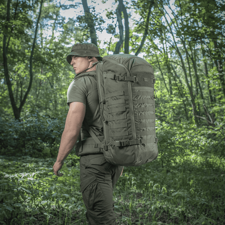 Mann med M-Tac Ryggsekk Gen.II Elite Large i skogterreng, ergonomisk design med slitesterk Cordura, ideell for friluftsliv og våpentransport.