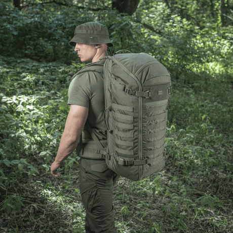 Mann bærer M-Tac Ryggsekk Gen.II Elite Large i skog. Ryggsekken viser slitesterkt Cordura-materiale, ideell for utendørs eventyr.