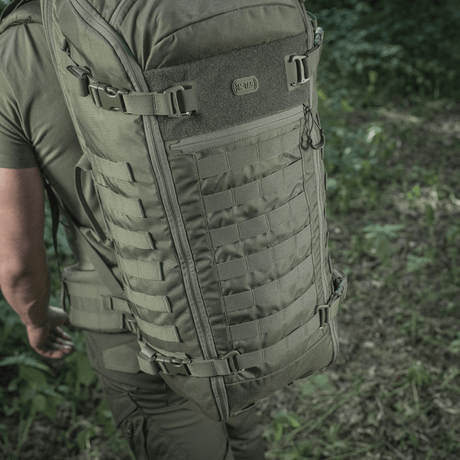 Person iført M-Tac Ryggsekk Gen.II Elite Large i naturen, viser sekkens slitesterke Cordura-design og romslige oppbevaringsmuligheter.