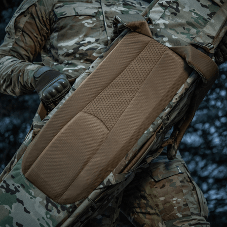 M-Tac Gun Backpack Case 125 cm Gen.II Elite i brug med camouflageudstyr, visning af ergonomisk polstret rygpanel, optimal til våbentransport.