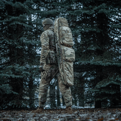 Person i skov med M-Tac Gun Backpack Case 125 cm Gen.II Elite, designet til sikker våbentransport, camouflage.