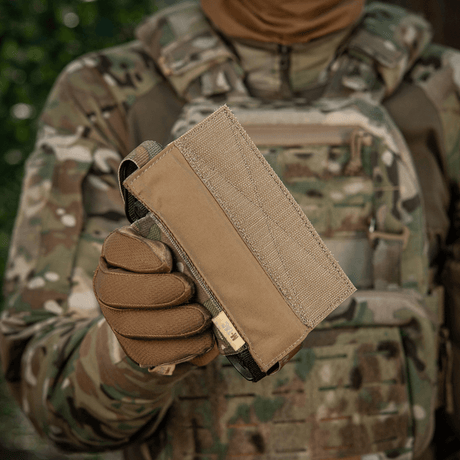 M-Tac Tourniquet Pouch Elastisk VELCRO Gen.II i camouflerte omgivelser, holdt av en person med taktisk utstyr.