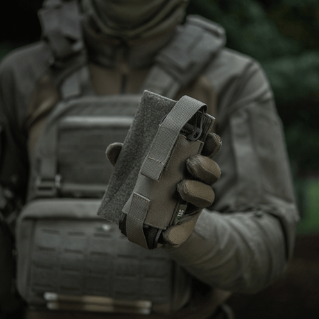 M-Tac Tourniquet Pouch Elastisk VELCRO Gen.II holdes av en taktisk utrustet person for rask tilgang til tourniquet