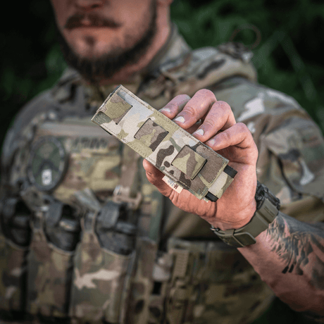 M-Tac Tourniquet Pouch Elastisk med MOLLE Gen.II i camo-design holdt av person med taktisk utstyr, viser lett tilgang og oppbevaring.
