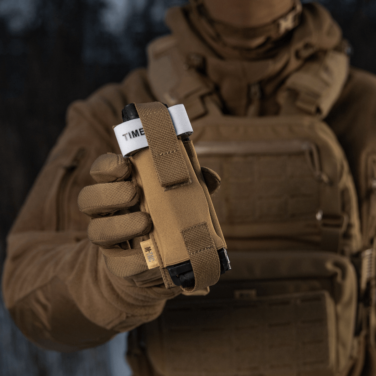 M-Tac Elastisk Tourniquet Pouch Molle Gen.III i brug i felten, fremhæver hurtig adgang og sikker fastgørelse af tourniquet.