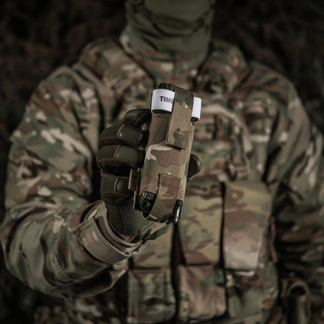 Soldat i kamuflasjeuniform holder M-Tac Elastisk Tourniquet Pouch Molle Gen.III foran for rask tilgang.