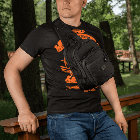 Mann iført M‑Tac Cross Bag Elite Hex, en slingveske av Cordura 500, perfekt for daglig bruk og taktisk utstyr.