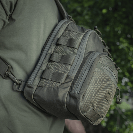 M-Tac Cross Bag Elite Hex sling-pack i Cordura 500, sett på skulderen i grønne omgivelser, perfekt for daglig bruk og taktisk utstyr. 5 liter.
