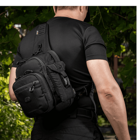 Mann bærer en svart M-Tac Smartphone Lomme Elite Large Hex laget av CORDURA HEX-materiale. Stilig design, perfekt for telefoner opptil 6,5 tommer.