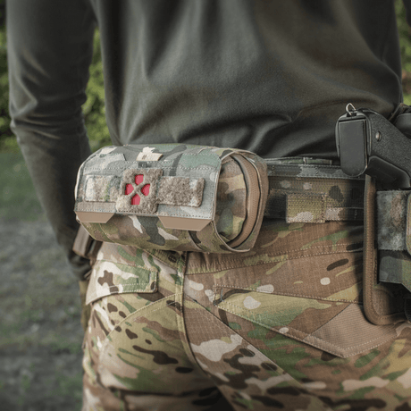 M-Tac Horizontal Medical Pouch Elite festet på kamuflasjeuniform i felten, ideell for førstehjelp med vanntett glidelås og organizer.