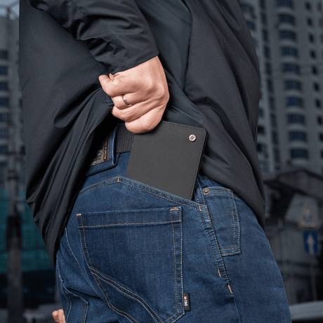 Person putter M‑Tac Pung Slim Elite i baklommen på jeans, kompakt og stilfullt design for kort og kontanter.