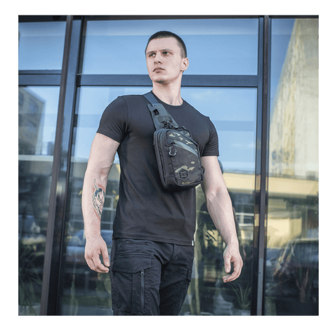 Mann med M-Tac Sling pistolveske Elite Hex foran en glassbygning, viser allsidighet og stil