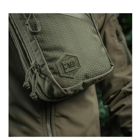 M-Tac Sling pistolveske Elite Hex på en person med jakke, laget i slitesterkt Cordura 1000D-materiale med justerbar rem.