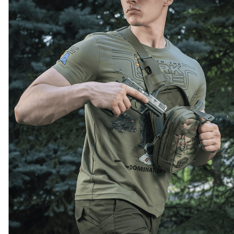 Mann bærer M-Tac Sling pistolveske Elite Hex med en skjult pistol i skogen.