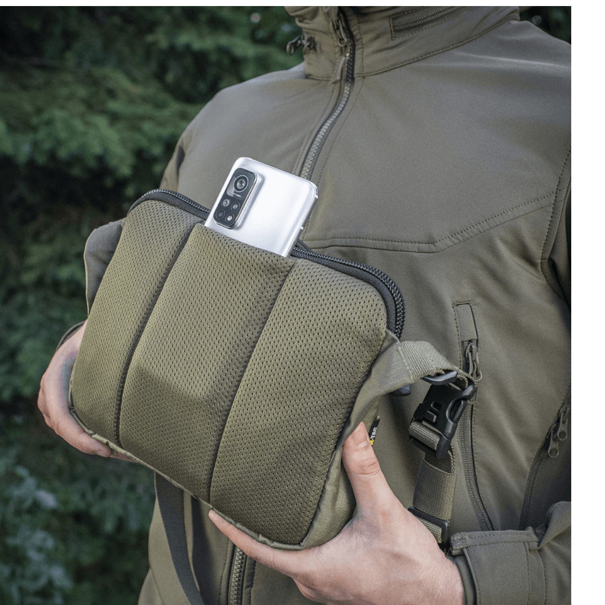 M-Tac Admin Taske Elite i Cordura stof, vist med en smartphone i lommen, justerbar skulderrem og solid konstruktion, udendørs baggrund.