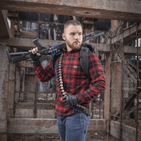 Mann bærer M-Tac Bandolier Elite og skytevåpen i industrielt miljø, designet for rask tilgang til ammunisjon.