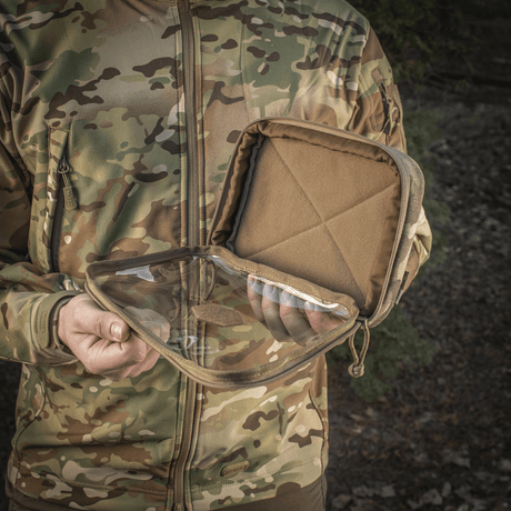 Mann holder M-Tac Utility Organizer Slim Elite med gjennomsiktig forvegg og robust Cordura 500D-materiale utendørs i kamuflasjejakke.