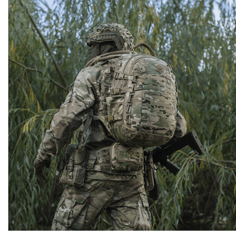 Soldat med M-Tac Mission Pack Elite ryggsekk i camouflage, i naturlig miljø.