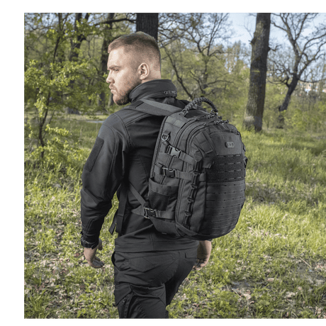 Mann bærer M-Tac Mission Pack Elite ryggsekk i naturen, fremhever det ergonomiske designet og slitesterkt Cordura 1000D-materiale.