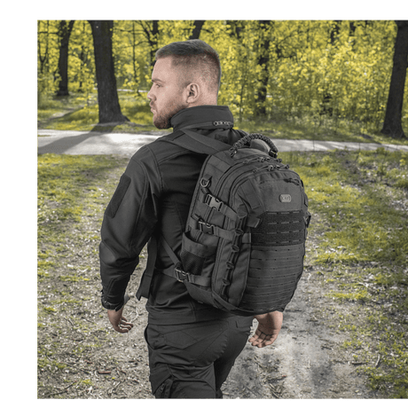 Mann bærer M-Tac Mission Pack Elite ryggsekk i skogmiljø, laget av slitesterkt Cordura 1000D med MOLLE LASER CUT-system.