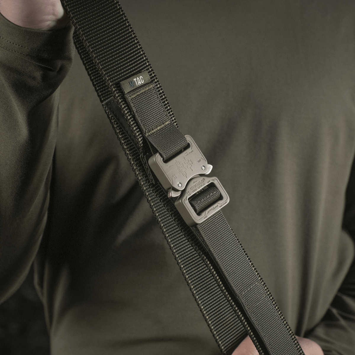 M-Tac Taktisk Bælte med Cobra-spænde holdt i hånden, fremstillet af slidstærkt nylon med Cobra 25 mm-spænde fra Austrialpin.
