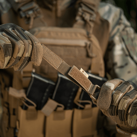 Person som demonstrerer bruk av M-Tac feste med D-ring på taktisk vest med MOLLE-system i utendørs miljø.