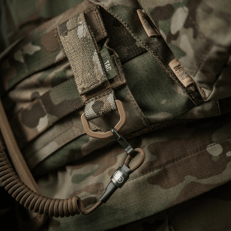 M-Tac feste med D-ring montert på camo-ryggsekk, ideell for taktisk bruk med MOLLE-system. Velcro-lukking, kompakt og lett design.