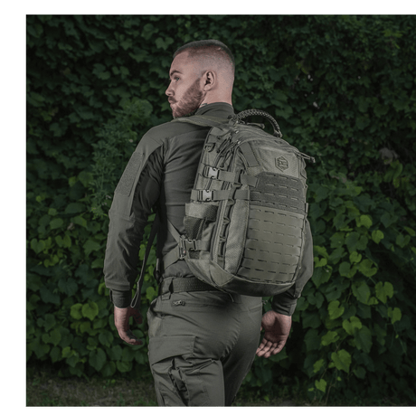 Person med en M-Tac Mission Rygsæk Elite Hex foran grønn vegetasjon.