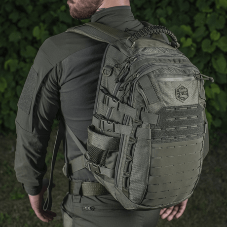 M-Tac Mission Rygsæk Elite Hex på ryggen av person i taktisk klær, med Cordura-materiale og MOLLE-system, sett bakfra i naturen.
