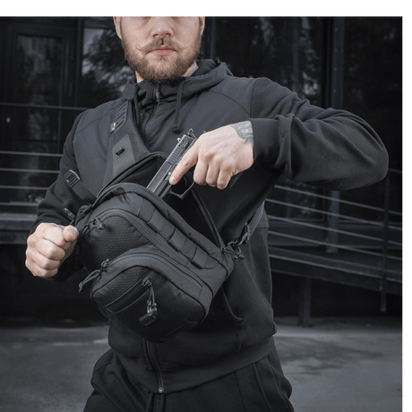 Mann iført M-Tac Cross Taske Slim Elite Hex i sort med Cordura-materialer, lynlåser og spenner fra YKK og Woojin, utendørs miljø.
