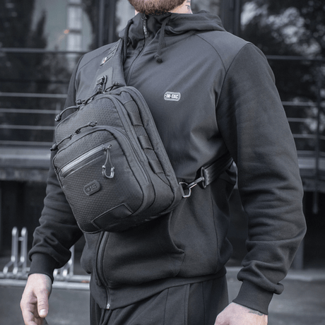 M-Tac Cross Taske Slim Elite Hex båret av en person i sort bekledning, utendørs miljø.