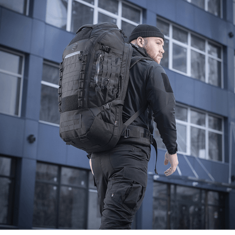 Mann bærer M-Tac Rygsæk Large Elite Hex Gen. IV i sort, ergonomisk designet for funksjonalitet og holdbarhet, sett i urbant miljø.