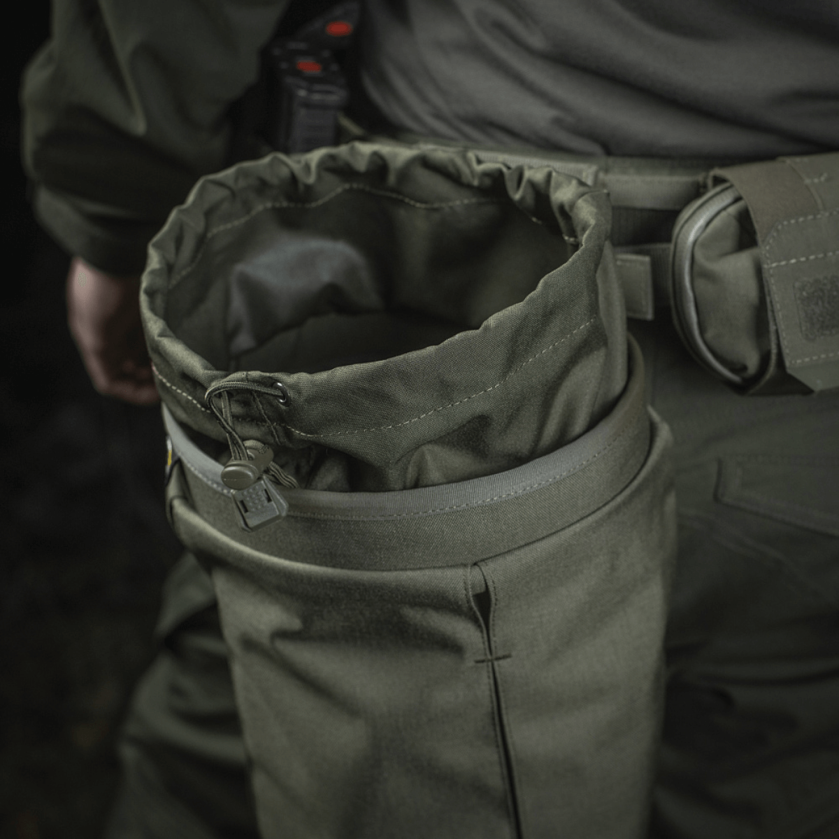 Person wearing M‑Tac Magasinsæk Dump Pouch Lite Elite in green Cordura 500D, attached to belt with MOLLE straps.