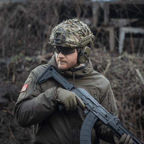 Person iført M‑Tac Vilha Hjelmcover FAST i Multicam, holder våpen i ujevnt terreng.