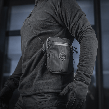 Person med M‑Tac Pocket Bag Elite HEX, en kompakt veske egnet for EDC-utstyr og nøkler, laget av slitesterkt materiale med YKK-glidelåser.
