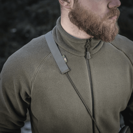 Mann bærer en grønn fleece med M‑Tac Pocket Bag Elite HEX-remmen over skulderen, viser holdbarhet og stil.