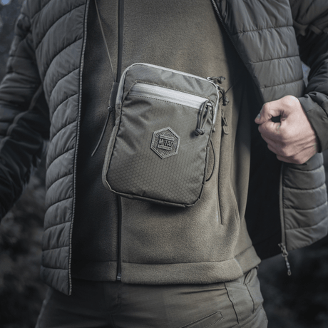 M‑Tac Pocket Bag Elite HEX bæres foran på en mann i utendørs bekledning, viser vesken kompakte og robuste design med YKK-glidelåser.