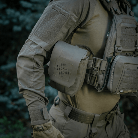 M-Tac Medic Pouch Vertical Large Elite montert på taktisk vest i skog, robust oppbevaring av førstehjelpsutstyr.