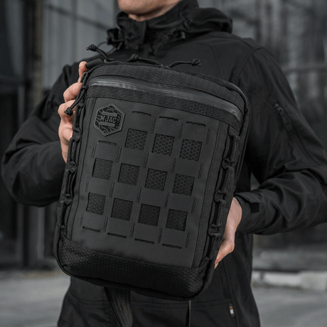 Mann holder en M-Tac Tablet Bag Laser Cut Hex i hånden, laget av Cordura-materialer med Laser Cut MOLLE-panel foran.