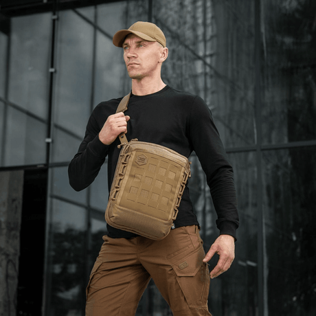 Mann bærer M-Tac Tablet Bag Laser Cut Hex foran kontorbygg, diskret skulderveske for EDC og dokumenter.