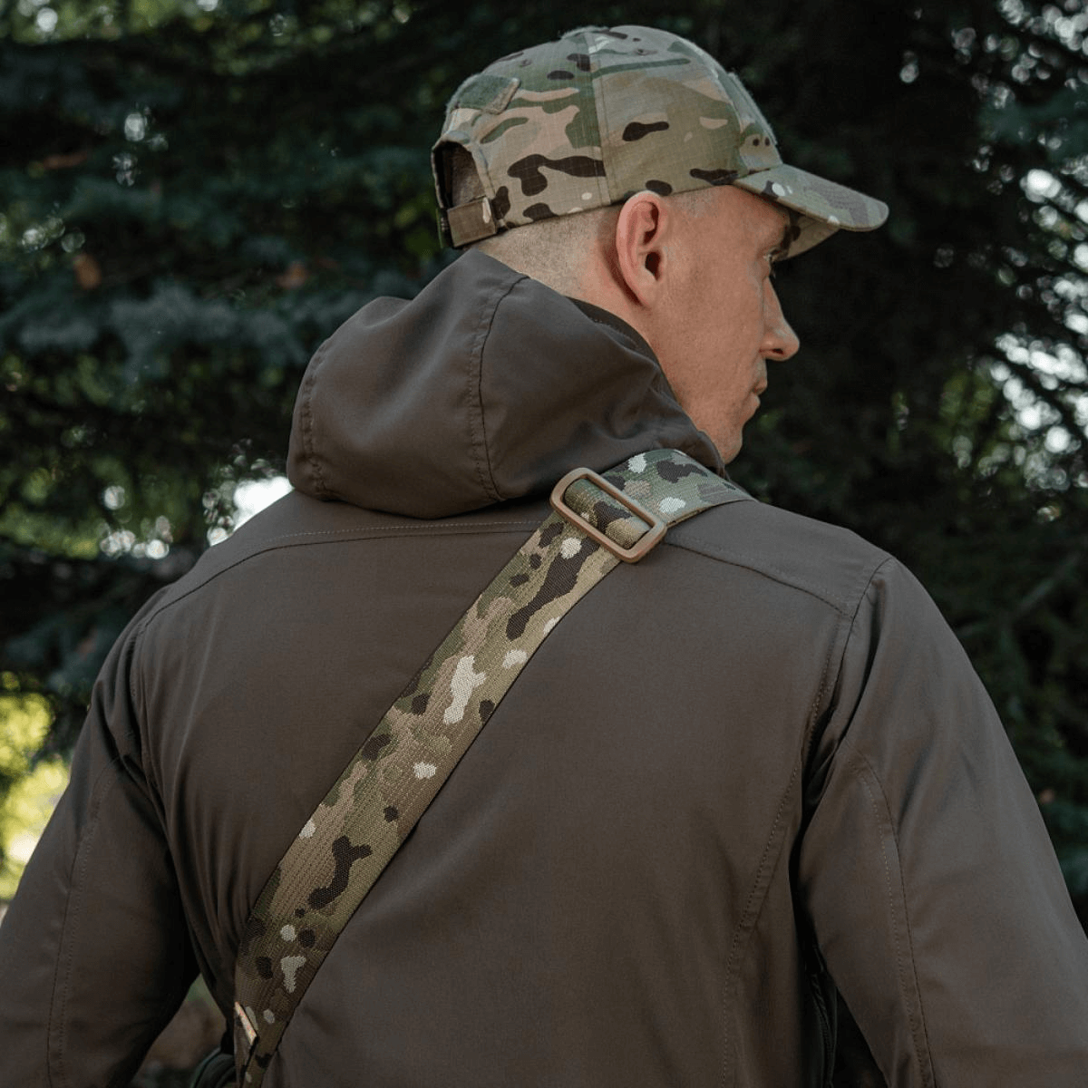 Person wearing a camo cap and jacket with a camouflage strap outdoors
