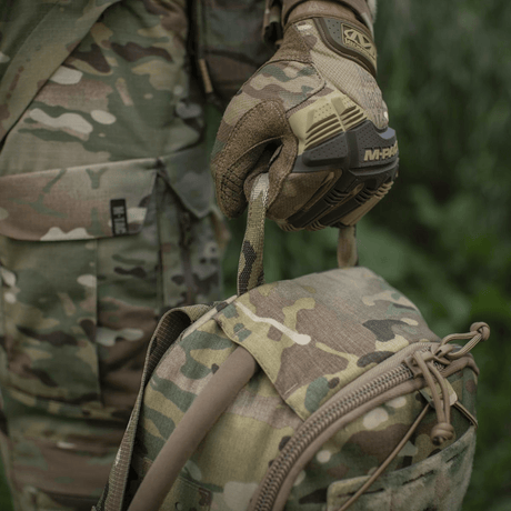 M-Tac STURM Elite ryggsekk i kamuflasjemønster med MOLLE system, holdt av person i militærklær og taktiske hansker, 15 liter kapasitet.